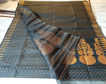 May include: Black and gold saree with a dotted pattern and floral border. The saree is made of a sheer fabric and has a decorative design on the border. The fabric is folded over, revealing the underside of the saree.