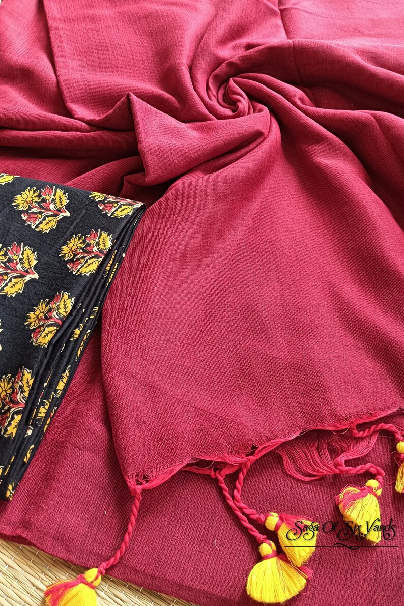 May include: A draped, deep red fabric with a textured appearance, paired with a folded black textile featuring a yellow and red floral pattern. The red fabric has tassels with yellow accents.