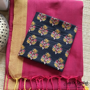 May include: A magenta textile with a gold border and a black patterned fabric. The black fabric has a repeating floral design in yellow and red. The magenta textile has a fringe with yellow and magenta tassels.