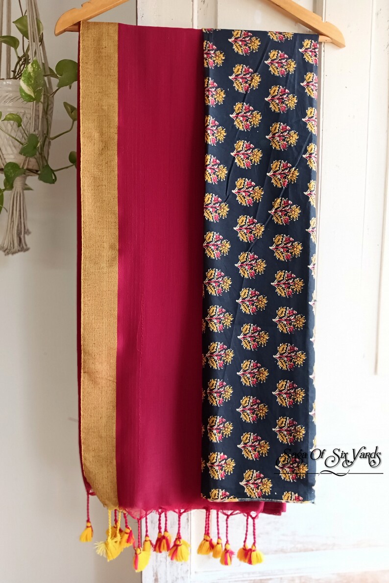 May include: A burgundy and navy blue scarf with a floral pattern and gold trim, hanging on a wooden hanger. The scarf has yellow tassels at the bottom. The right side of the scarf has a navy blue background with a yellow and red floral pattern.