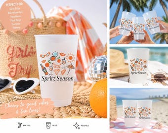 May include: A white reusable 16 oz plastic cup featuring a colorful graphic print of sunglasses, citrus slices, cocktails, and a beach umbrella with the text Spritz Season printed in black. The cup is shown in multiple settings including a beach.