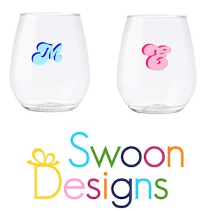 May include: Two clear glass wine glasses with a blue "M" and a pink "E" on them. The glasses are on a white background with the text "Swoon Designs" in colorful letters below them.