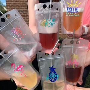 K&ouml;nnte beinhalten: Transparente Getr&auml;nkebeutel aus Kunststoff mit verschiedenen bunten Designs und Namen, darunter "Robin", "Ashley", "Whitney" und "Kellie". Jeder Beutel enth&auml;lt ein andersfarbiges Getr&auml;nk und einen Edelstahlstrohhalm. Die Beutel werden von mehreren Personen gehalten.