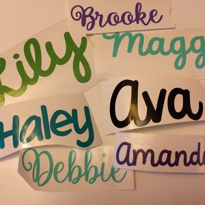May include: A collection of personalized vinyl stickers with names written in a cursive font. The names include Lily, Haley, Debbie, Ava, Amanda, Maggie, and Brooke. The stickers are on a white background.