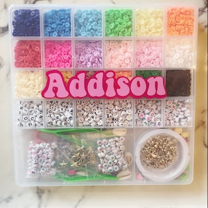 May include: A clear plastic storage box filled with colorful beads and letters. The box has a pink and white name tag that reads "Addison".