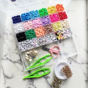 May include: A clear plastic organiser filled with colourful beads, including letter beads and smiley face beads. Also included are pink scissors, green tweezers, and small bags of jewellery-making supplies. The beads are arranged in a variety of colours.