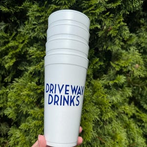 May include: A stack of white plastic cups with the text "DRIVEWAY DRINKS" printed in blue on the front.