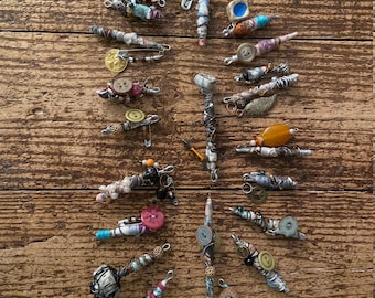 May include: A collection of 18 handmade wire wrapped pins with various embellishments, including buttons, beads, and charms. The pins are displayed on a wooden surface.