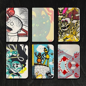 May include: Six small, square, colorful notebooks with different cartoon illustrations. The notebooks have white covers with black outlines. The illustrations include a man with a red phone, a green monster, a man with a chain, two men on a platform, a man in a spacesuit, and a red and blue monster.