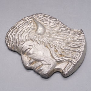 May include: A silver-colored metal sculpture of a person's head with a single horn on the forehead. The sculpture is detailed with textured hair and facial features.