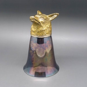 May include: A silver and gold fox head topper for a drinking cup. The cup is made of silver and has a dark, iridescent finish.