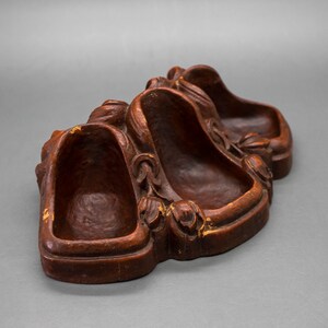 May include: A wooden trinket dish with three carved depressions. The dish is a dark brown color with a slightly reddish hue. The dish is decorated with carved floral designs.