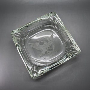 May include: A clear glass ashtray with an etched design of an American bald eagle with a shield and stars.