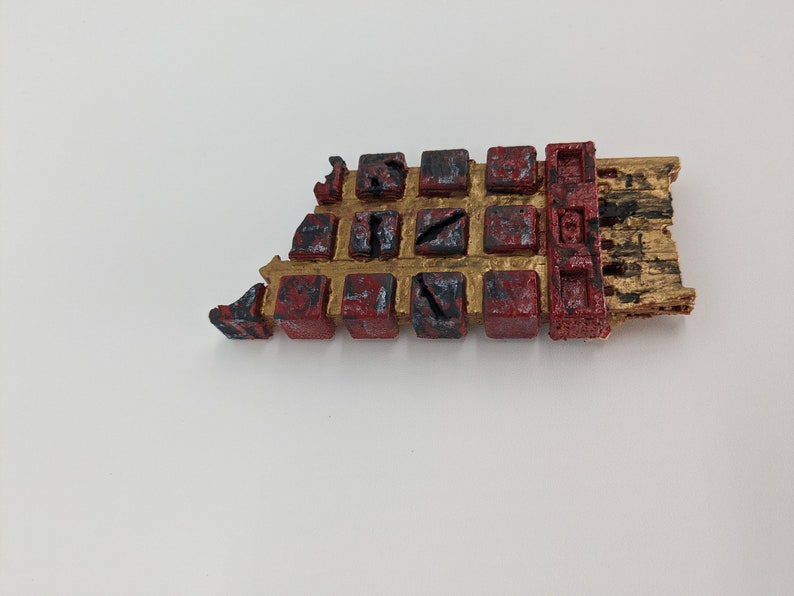 May include: A 3D printed, gold and red, segmented, rectangular object with black markings. The object is broken in the upper left corner.