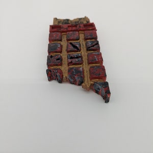 May include: A small, rectangular, red and gold-painted wooden object with a grid of squares. Each square has a different symbol or design.