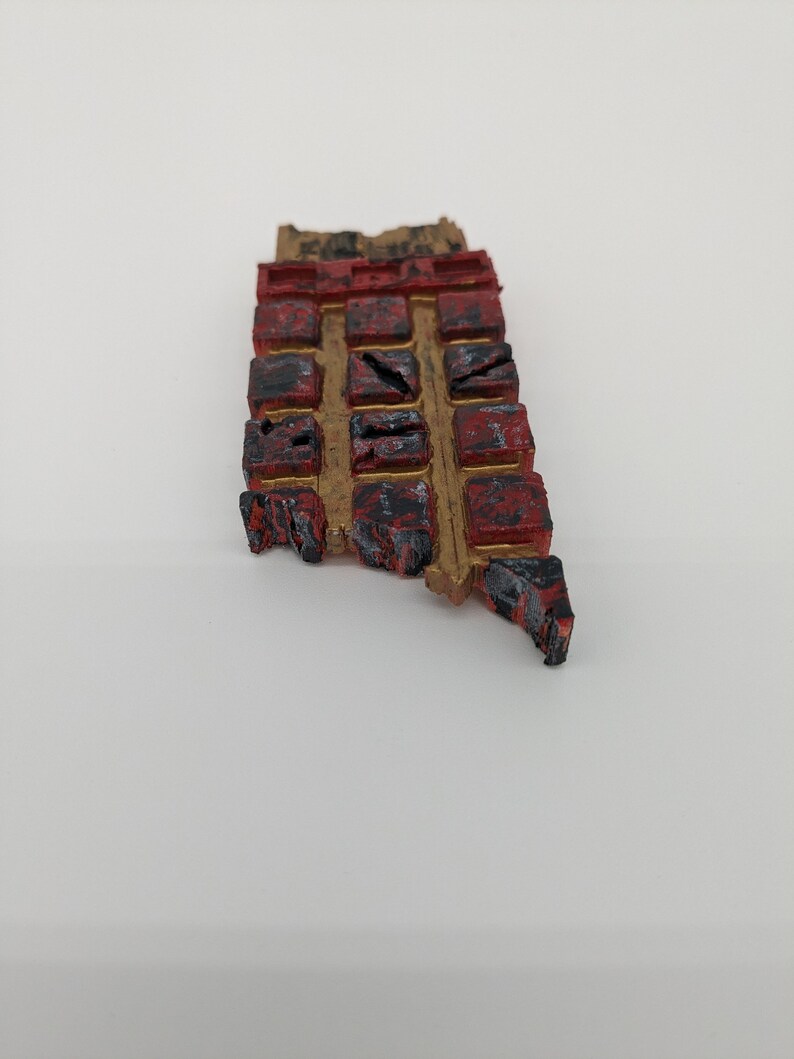 May include: A small, rectangular, red and gold-painted wooden object with a grid of squares. Each square has a different symbol or design.