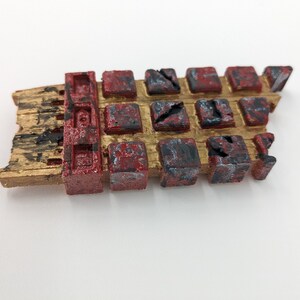 May include: A broken, gold-painted, rectangular object with a red and black grid pattern. The object is made of a textured material and has a rough, weathered appearance.