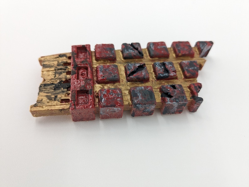 May include: A broken, gold-painted, rectangular object with a red and black grid pattern. The object is made of a textured material and has a rough, weathered appearance.