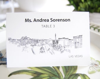 May include: White place card with black text that reads "Ms. Andrea Sorenson, Table 3, Las Vegas". The card features a black and white line drawing of the Las Vegas skyline.