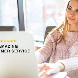 May include: A white laptop screen displaying five yellow stars and the black text AMAZING CUSTOMER SERVICE. The screen is positioned in front of a person wearing a light pink knitted jumper, who is looking toward the side of the laptop.