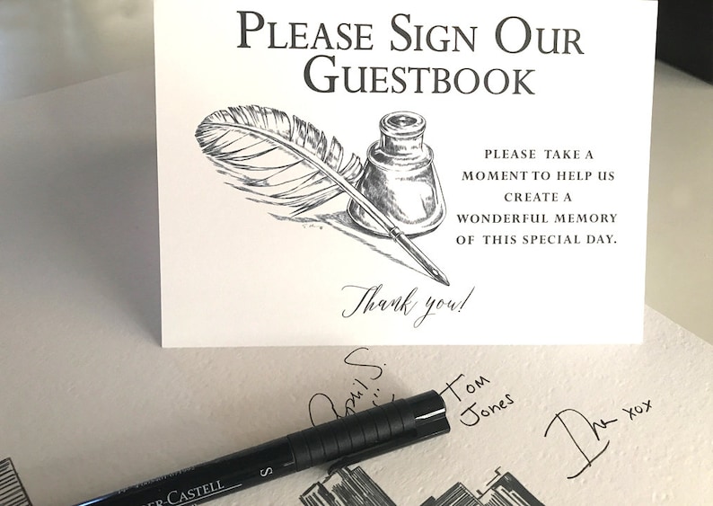 May include: A white rectangular sign with black text reading Please Sign Our Guestbook, followed by a black and white ink illustration of a quill and inkwell, and text reading Please take a moment to help us create a wonderful memory of this special day. Thank you!