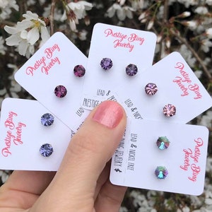 Op de afbeelding: Vijf kaarten met de tekst "Prestige Bling Jewelry" erop. Elke kaart heeft twee kleine oorbelletjes met verschillende gekleurde strass steentjes. De oorbelletjes zijn lood- en nikkelvrij.