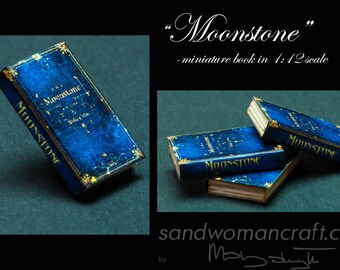May include: A miniature book titled "Moonstone" with a blue cover and gold lettering. The book is 1:12 scale.