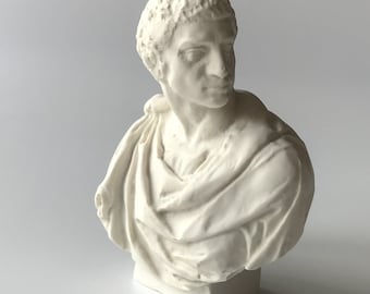 May include: White plaster bust sculpture of a man with short hair, wearing a toga-like garment. The bust is on a white rectangular base.