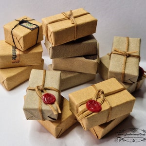 May include: A collection of miniature brown cardboard boxes tied with twine and sealed with red wax. The boxes are stacked and arranged on a white surface.