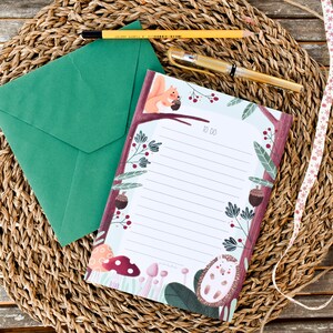 May include: A green envelope and a notepad with a woodland theme. The notepad has a white background with lined paper and a border of illustrations of a squirrel, mushrooms, berries, and a hedgehog. The notepad has the words "To Do" printed on it.