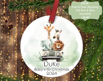 Puede incluir: Un adorno navideño redondo blanco con un diseño de acuarela de una jirafa, una cebra, un elefante y un león que van en un jeep verde. El adorno tiene el texto "Duke Baby's 1st Christmas 2024" impreso en él.