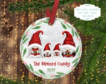 May include: A white round Christmas ornament with a green wreath border. Three gnomes are depicted in the center, with the text "The Menard Family 2022" below.