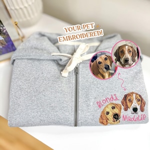 May include: A gray zippered hoodie with two embroidered dog portraits. The dogs are a brown and white dachshund named "Blondi" and a brown and white beagle named "Maddie".