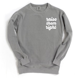 May include: A gray sweatshirt with the phrase "raise them right" printed in white on the front.