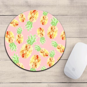 May include: A pink round mouse pad with a repeating pattern of yellow and orange pineapples. The pineapples are drawn in a watercolor style.