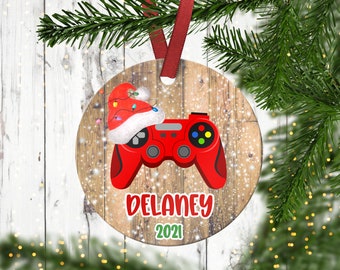 May include: Red and white Christmas ornament with a video game controller, a Santa hat, and the name Delaney 2021.