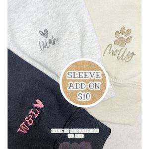 Op de afbeelding: Close-up van drie sweatshirtmouwen in grijs, cr&egrave;me en zwart. Elke mouw heeft geborduurde details: een naam met een hart, een pootafdruk met een naam en initialen met een hart. Een cirkelvormige afbeelding leest "SLEEVE ADD-ON".