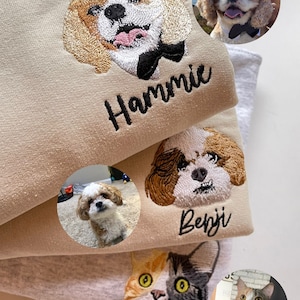 Op de afbeelding: Geborduurde petportret sweatshirts in beige en grijs. Elke sweatshirt heeft een op maat geborduurde afbeelding van een hond of kat, met de naam van het huisdier eronder. De afbeelding bevat een hond met een zwarte strik.