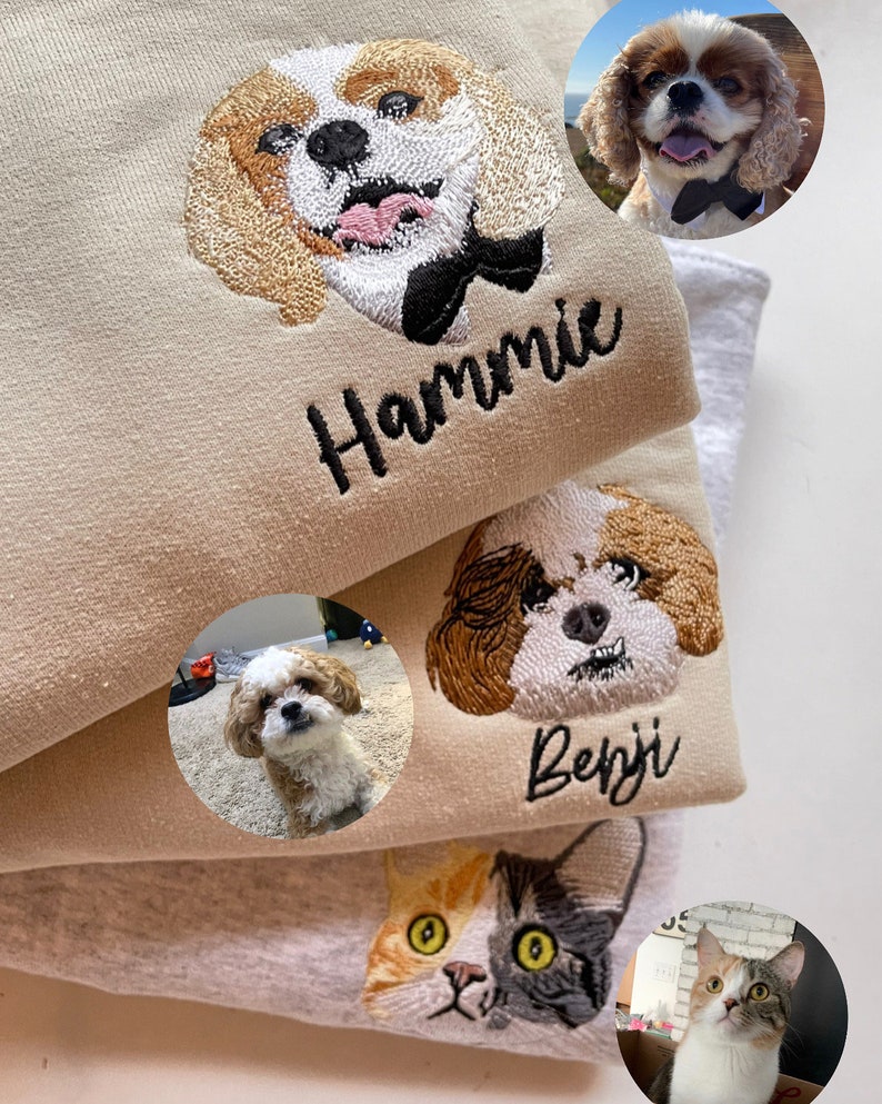 Op de afbeelding: Geborduurde petportret sweatshirts in beige en grijs. Elke sweatshirt heeft een op maat geborduurde afbeelding van een hond of kat, met de naam van het huisdier eronder. De afbeelding bevat een hond met een zwarte strik.