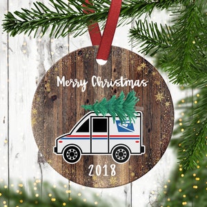May include: A round wooden Christmas ornament with a white mail truck carrying a small Christmas tree on top. The ornament has a rustic wood grain texture and the text "Merry Christmas 2018" is printed on it.