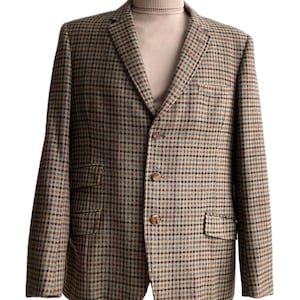 May include: A brown and tan checked blazer with a three-button fastening and two front pockets. The blazer is worn with a tan roll neck. The label "kuhl vintage" is in the top left corner.