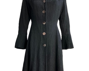 Può includere: Un cappotto nero a maniche lunghe con vita stretta e gonna svasata. Il cappotto ha un colletto alto e una chiusura con bottoni. Il tessuto ha un motivo testurizzato.
