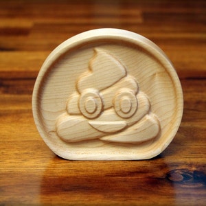 May include: A wooden carving of a smiling poop emoji. The carving is light brown and has a detailed design.