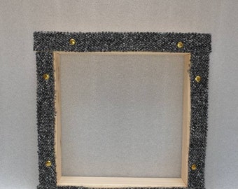 May include: Square wooden picture frame with a dark gray textured border. The frame is adorned with small gold-colored studs at each corner. The interior is empty, ready for a photo or artwork.