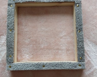May include: A wooden frame with a gray fabric border and gold tacks. The frame is empty and ready for a piece of art.