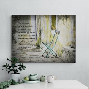 May include: A canvas print with a distressed, vintage-style image of a weathered, green metal chair sitting on a stone path. The background is a yellow and green wall with peeling paint. The print features a Bible verse from Deuteronomy 31:8, which reads: "And the Lord, He it is that doth go before thee; He will be with thee, He will not fail thee, neither forsake thee: fear not neither be dismayed."