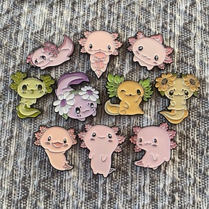 May include: Set of ten enamel pins featuring axolotls in various poses and colours. The axolotls are wearing flowers, hats, and other accessories. The pins are perfect for adding a touch of whimsy to your backpack, jacket, or bag.