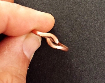 Op de afbeelding: Een koperen ring met een uniek, verweven ontwerp. De ring wordt van de zijkant getoond, waardoor de ingewikkelde details van het metaalwerk worden benadrukt.