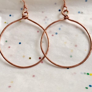 May include: A pair of copper hoop earrings with a hammered finish. The earrings are simple and elegant, and would make a great gift for any occasion.