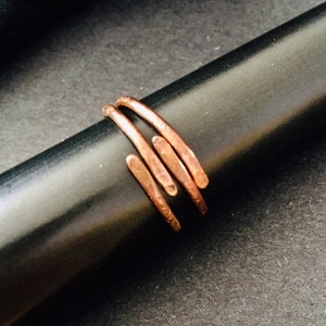 May include: A copper ring with a hammered finish. The ring is made of three thin bands of copper that are twisted together.